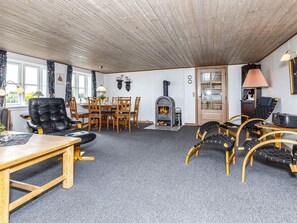 A cozy room with a fireplace, a dining table with chairs, and a seating area with cushioned chairs. - 6 Person Holiday Home in Thisted (Thisted)