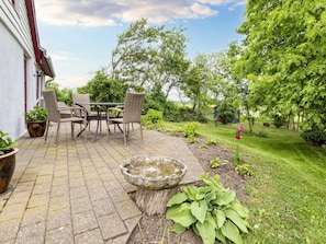 An outdoor patio with a table and chairs, surrounded by greenery and a stone birdbath.