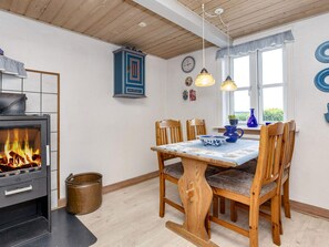 A dining area with a wooden table and chairs, a fireplace, and a view through the window. - 6 Person Holiday Home in Thisted (Thisted)