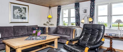 A living room with a sofa, a wooden coffee table, a black leather chair, and a view of the outdoors through large windows.