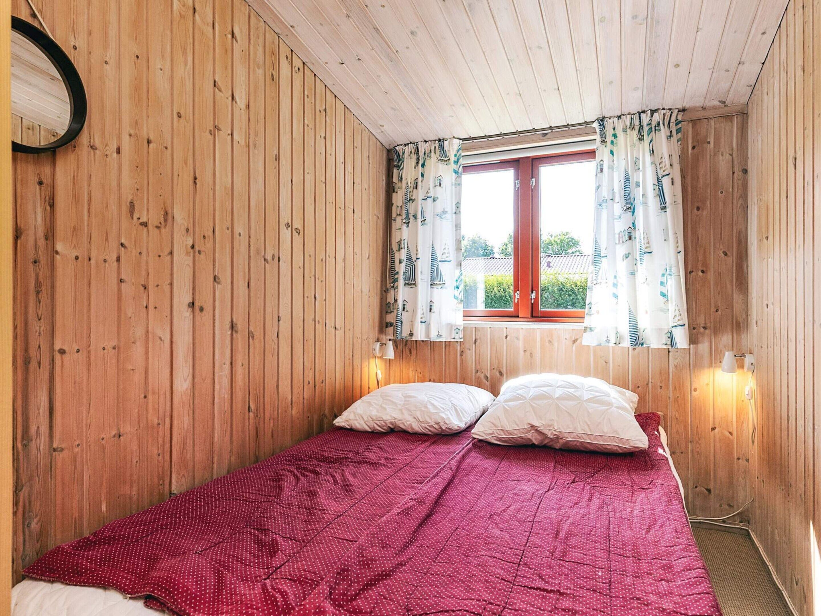 Ein Zimmer mit Holzvertäfelung, einem Bett, zwei Nachttischlampen und einem Fenster mit Vorhängen.