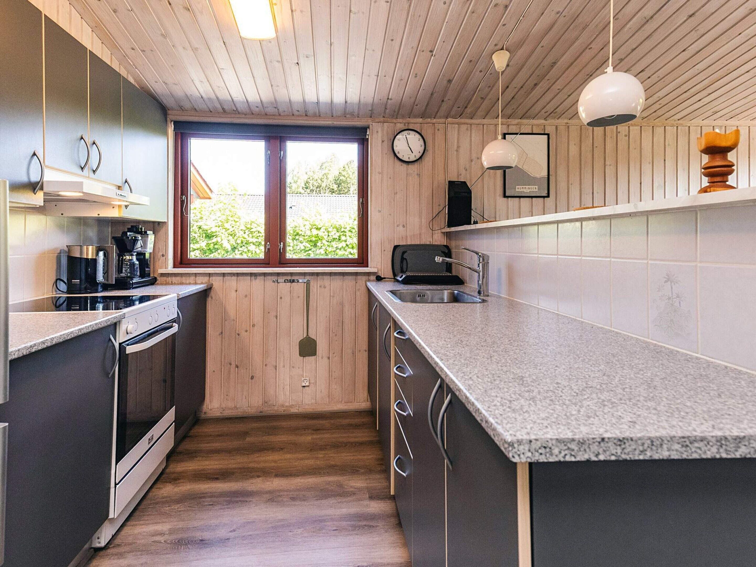 Eine moderne Küche mit Holzverkleidung, einem großen Fenster, einem Einbauofen, einer Spüle und einer Arbeitsplatte.