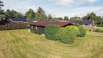 A residential property with a well-maintained lawn, a house with a red roof, and a large bush in the front yard.