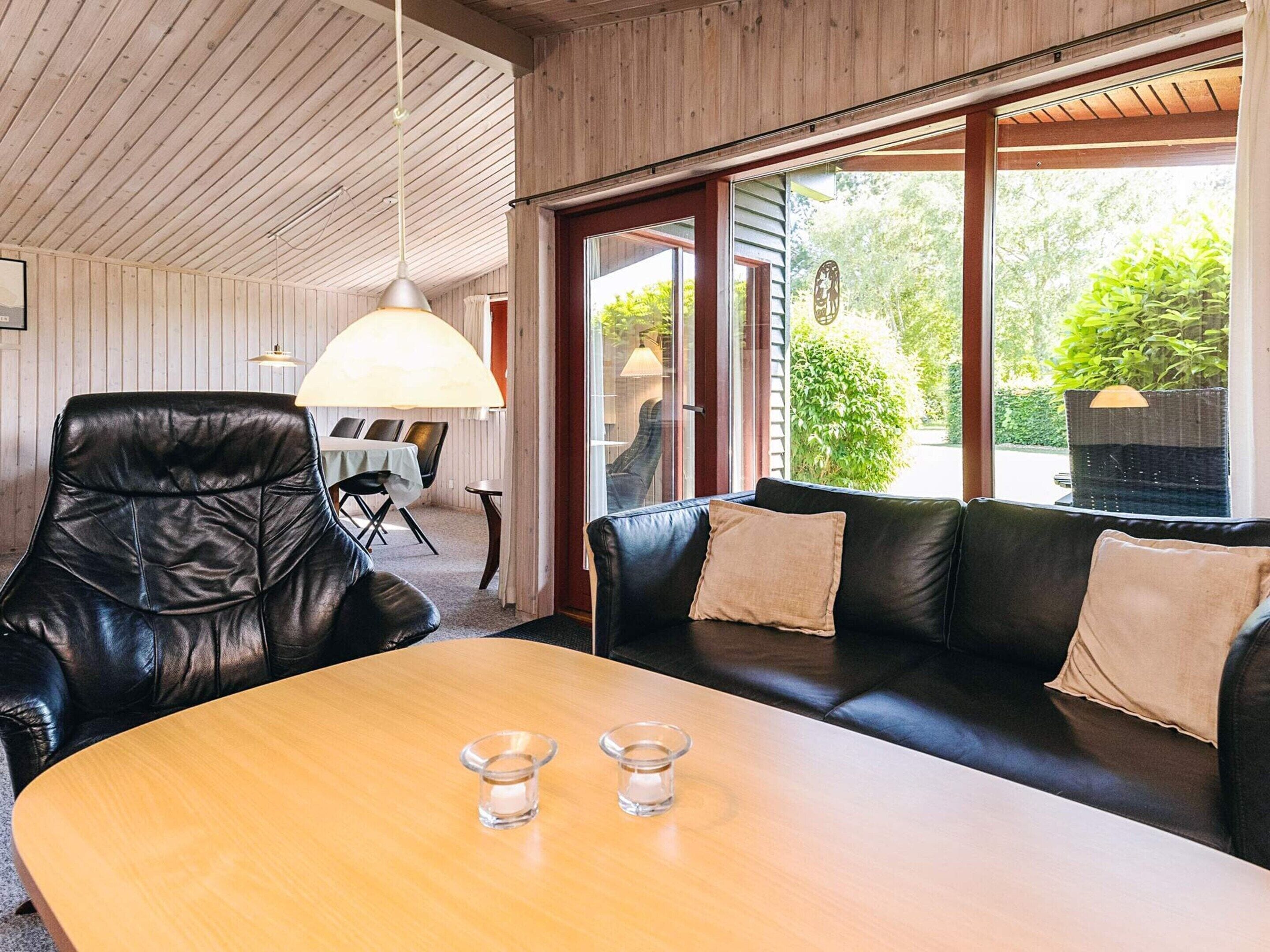A modern living room with a wooden ceiling, a black leather sofa, a wooden dining table, and a glass coffee table.