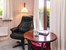 Et værelse med en læderstol, et træbord, en lampe og udsigt til grøn natur.