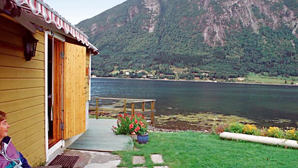 A wooden cabin with a porch overlooking a lake, surrounded by mountains. - 4 Person Holiday Home in Vistdal (Molde)