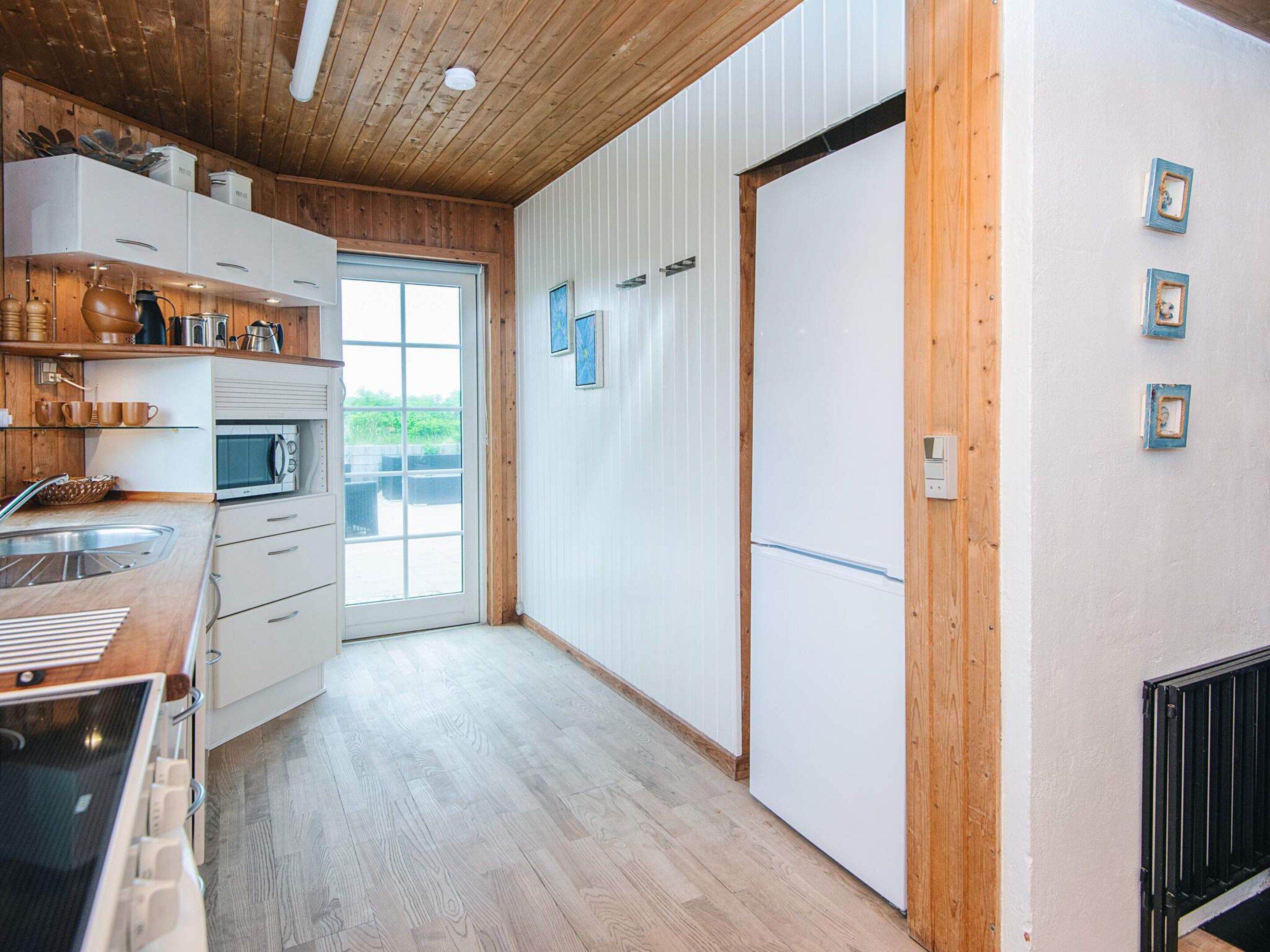 Una cocina con armarios de madera, microondas y un ventanal amplio.