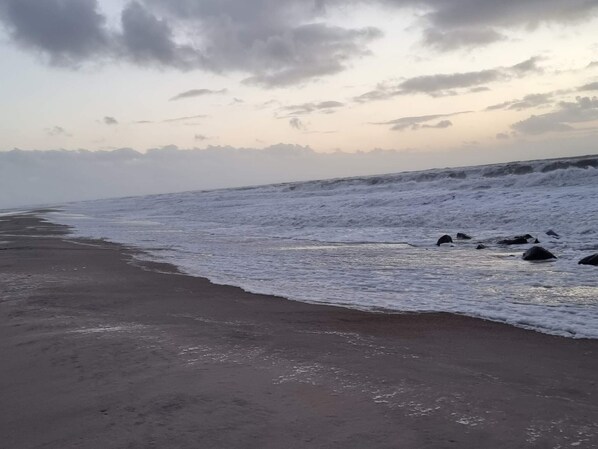 Una playa con olas, cielo despejado y montañas a lo lejos.