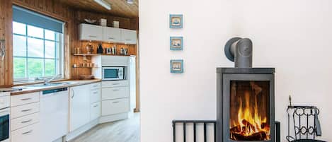 A modern kitchen with white cabinets, a microwave, and a wood-burning stove.