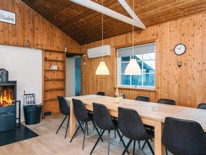 Un interior de madera con una larga mesa, sillas, una chimenea y un reloj en la pared.