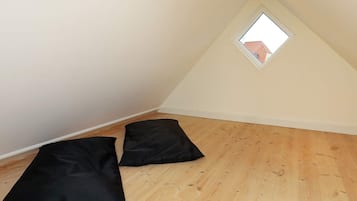 Una habitación con techo inclinado, un ventanal pequeño y dos cojines negros sobre el suelo de madera.