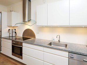 A modern kitchen with a built-in oven, a stainless steel range hood, a coffee maker, and a sink with a faucet.