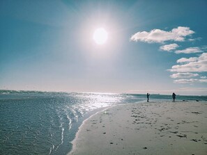 Una playa con cielo despejado, el sol brillando y huellas en la arena.