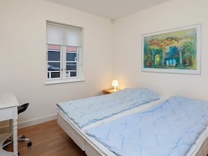 A bedroom with a bed, a desk, a window, and a painting on the wall.
