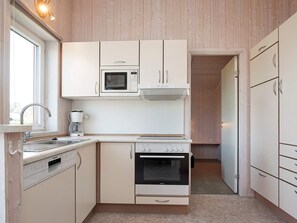A compact kitchen with white cabinetry, a built-in microwave, a coffee maker, and a dishwasher.