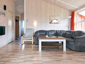 Una sala moderna con piso de madera, un sofá de cuero gris, una mesa de centro de madera y un televisor montado en la pared.