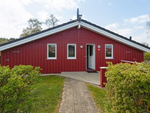 A red building with a white door and windows, a satellite dish on the roof, and a paved pathway leading to the entrance. - Holiday Home in GrÃ¶mmitz (Groemitz)