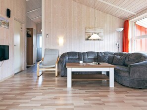 A modern living room with a wooden floor, a grey leather sofa, a wooden coffee table, and a television mounted on the wall. - Holiday Home in GrÃ¶mmitz (Groemitz)