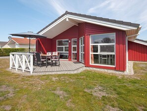 Een rode woning met een terras, een eettafel met stoelen en een groot raam.