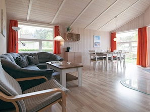 Uma sala de estar aconchegante com sofá, uma mesa de jantar e cadeiras. Teto de madeira e mesa de vidro na área de refeições.