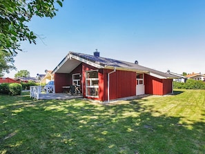 A red single-story house with a covered porch, a satellite dish, and a small garden area. - Holiday Home in GrÃ¶mmitz (Groemitz)