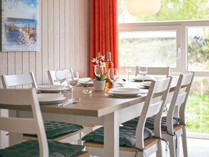 A dining area with a wooden table set for four, white chairs, and a window with a view of greenery. - Holiday Home in GrÃ¶mmitz (Groemitz)