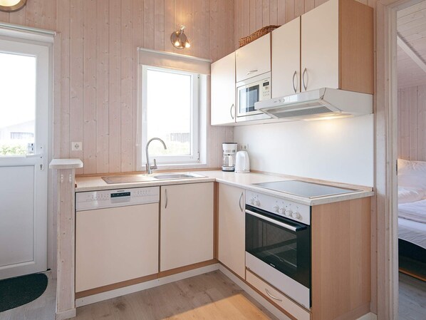 A compact kitchen with a dishwasher, microwave, stove, and a window providing natural light.