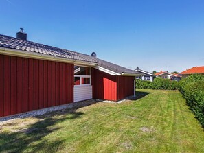 A red building with a white door and a small window, surrounded by a well-maintained lawn and a hedge.