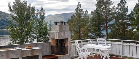 Une terrasse dotée d’un barbecue et d’un espace salon offrant une vue sur un lac et des montagnes.