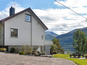 A white two-story house with a visible number '1052' on the side, a small porch, and a view of mountains and a lake. - 4 Star Holiday Home in Eidsvag (Molde)