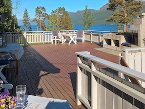 A wooden deck with outdoor furniture, a table with a lace tablecloth, and a view of a lake and mountains in the background. - 4 Star Holiday Home in Eidsvag (Molde)