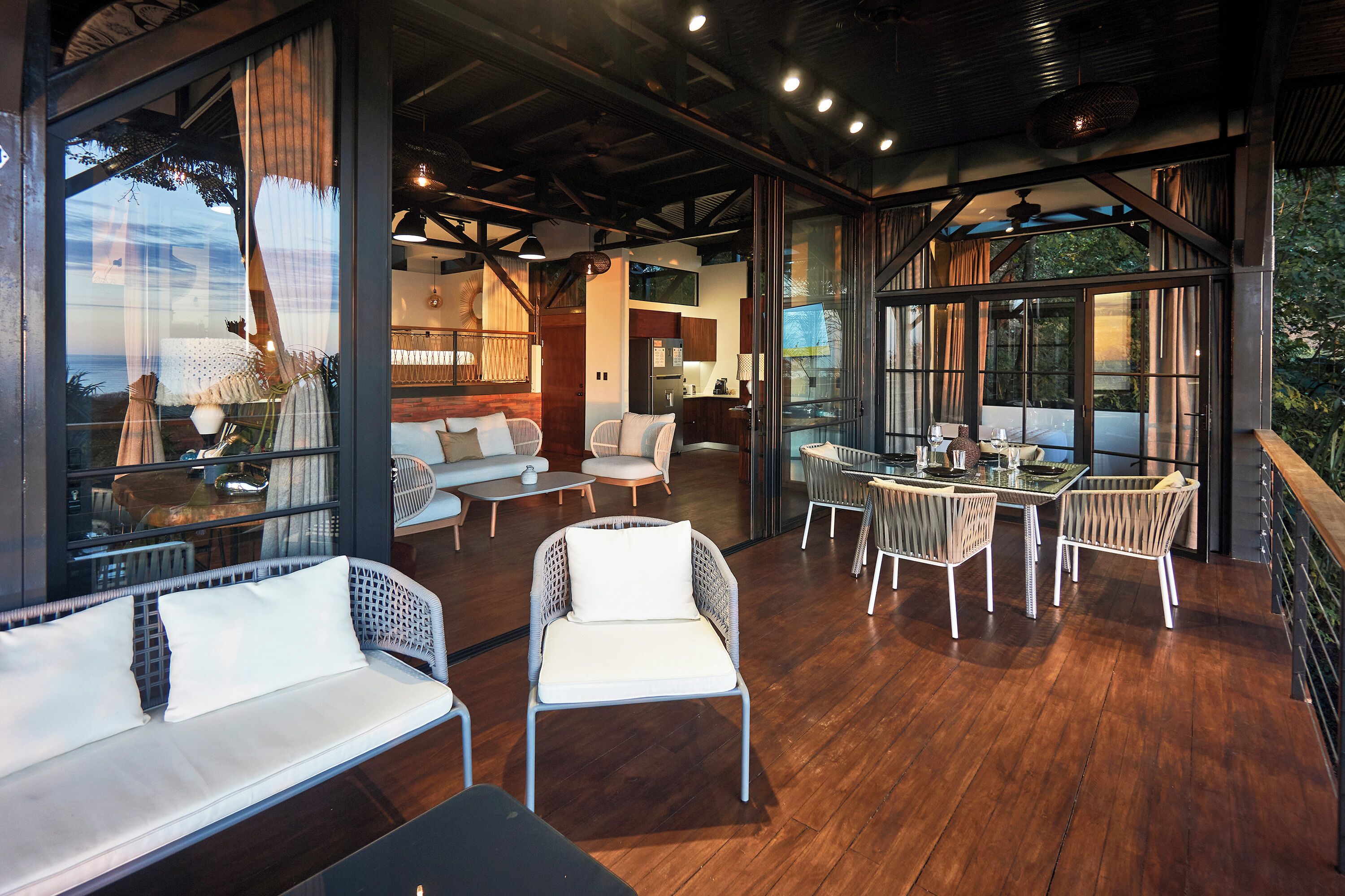 Un espacio interior amplio con piso de madera, muebles blancos y ventanas grandes que ofrecen vistas al exterior.