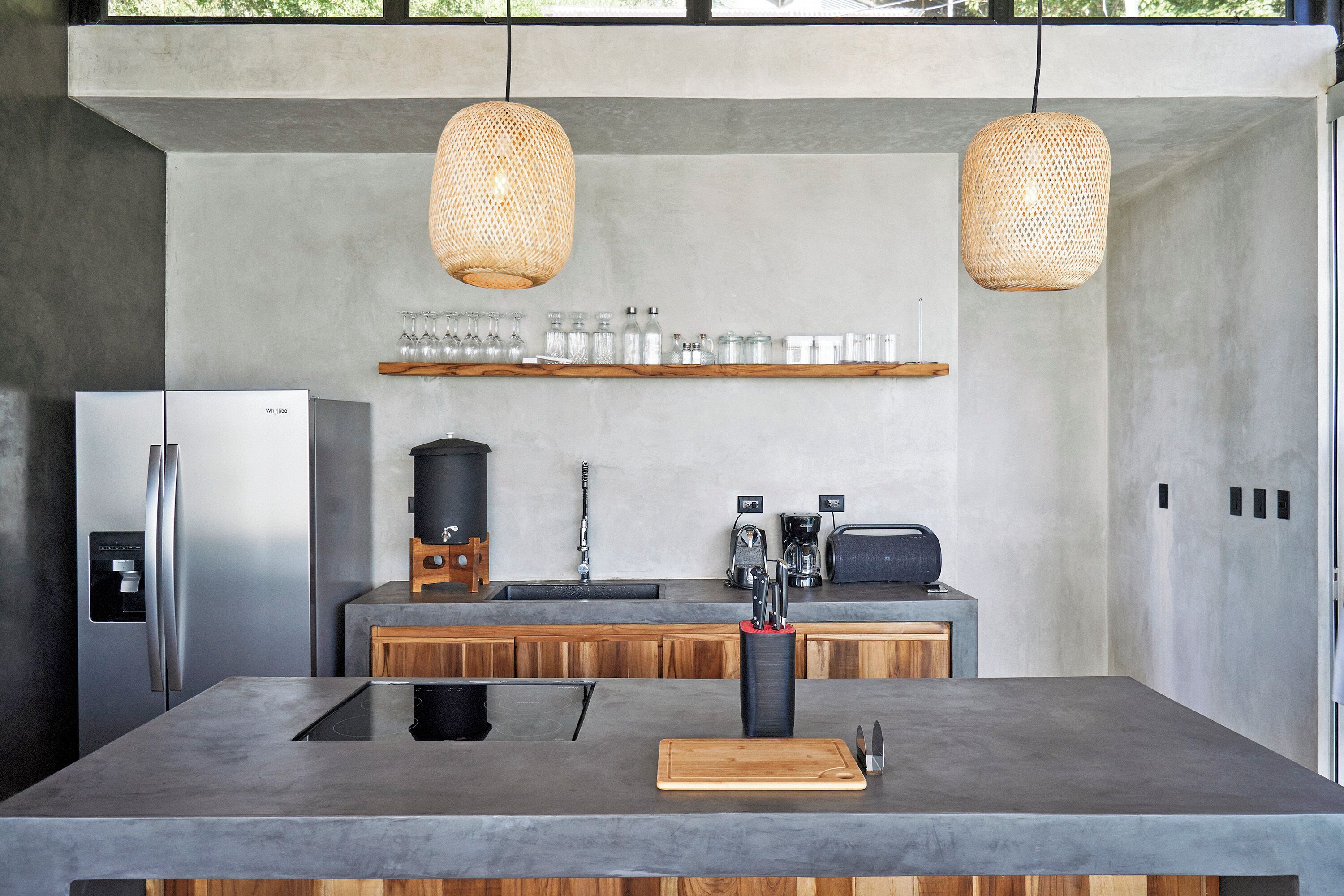 Une cuisine moderne dotée d’un grand îlot central, d’appareils électroménagers en acier inoxydable, de meubles en bois et de luminaires suspendus en osier.