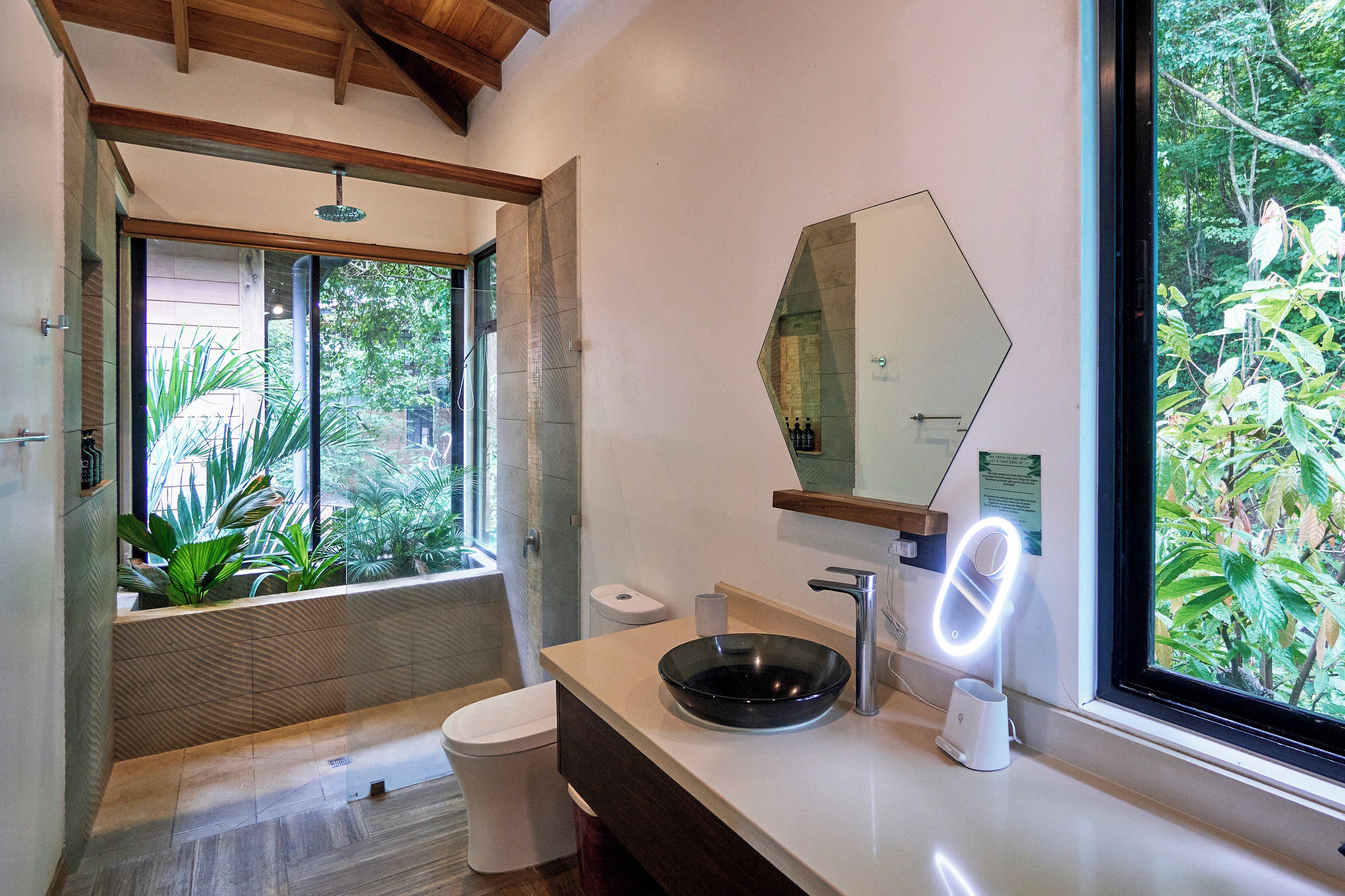 Un baño moderno con un ventanal grande, un lavabo redondo y un espejo con luz.
