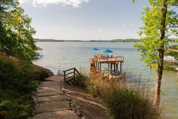 A wooden dock leading to a small wooden structure with a roof, surrounded by trees and a calm lake.