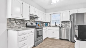 A modern kitchen with white cabinets, a stainless steel refrigerator, and a tiled backsplash.