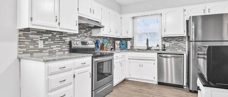 Enjoy cooking in this well-lit kitchen with a stainless steel refrigerator, oven, and white cabinetry.