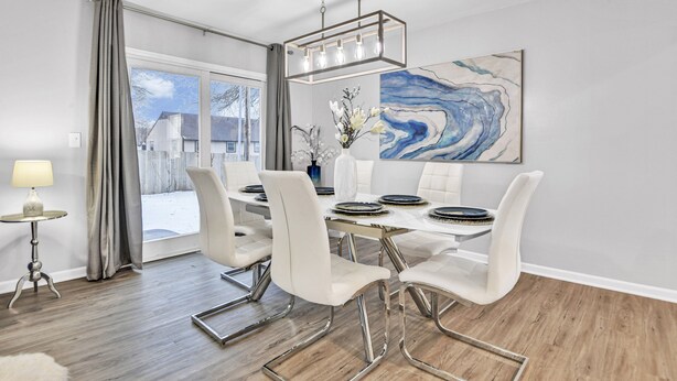 A dining area with a modern table and chairs, a chandelier, and a large abstract painting on the wall.