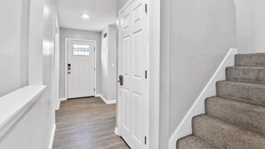A hallway with white walls, a wooden floor, and a staircase with grey carpet.
