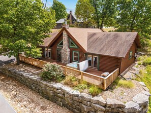 A log cabin with a stone chimney, a deck, and a stone wall surrounding the property.