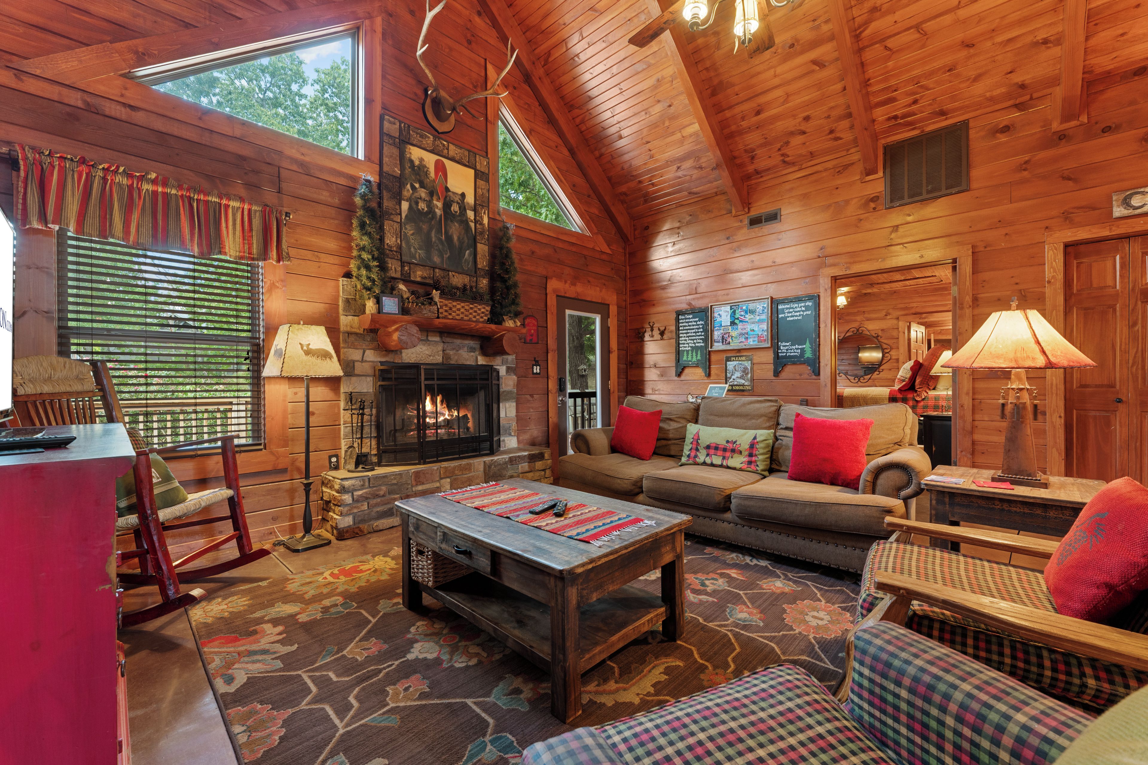 A log cabin interior with a fireplace, wooden furniture, and a large window.