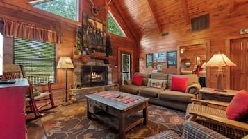 A log cabin interior with a fireplace, wooden furniture, and a large window.