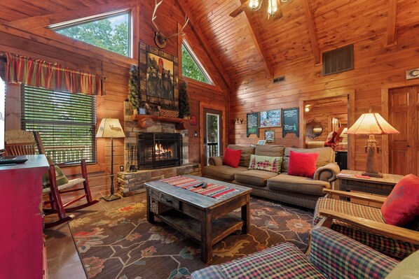 A log cabin interior with a fireplace, wooden furniture, and a large window.