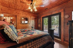 A wooden cabin bedroom with a large bed, a ceiling fan, and a view of the outdoors through a window.