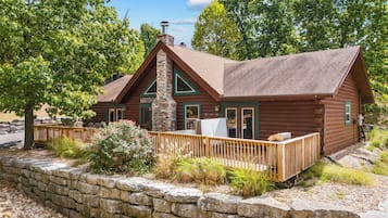 A log cabin with a stone retaining wall, a wooden deck, and a welcoming sign.