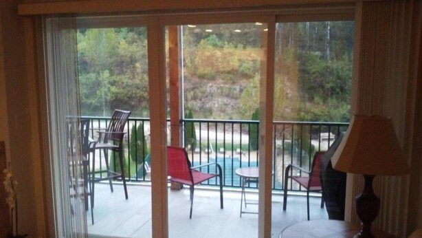 A room with a sliding glass door leading to an outdoor area with a pool, chairs, and a table. - Cedar Heights 464 (Camdenton)