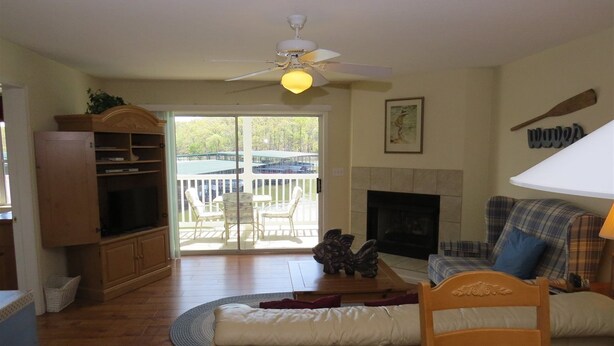 A living room with a fireplace, a ceiling fan, a television, and a view of the outdoors. - Parkview BAY 113 (Osage Beach)