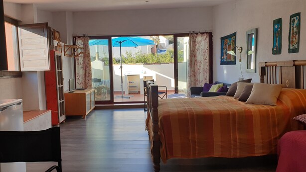 Ein Schlafzimmer mit Bett, Schreibtisch, Sessel, Sofa und einem Balkon mit blauem Sonnenschirm.