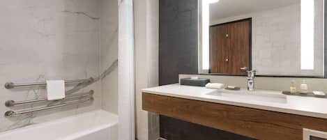 A modern bathroom with a marble wall, a wooden vanity, a large mirror, and a bathtub.
