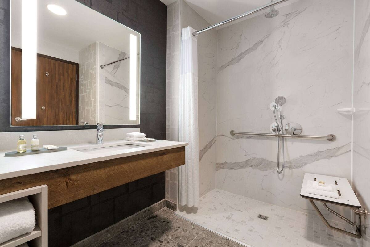 A modern bathroom with a marble shower, a wooden vanity, and a large mirror.